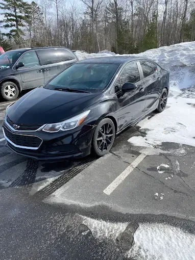 A black chevrolet cruze is parked in a snowy parking lot.