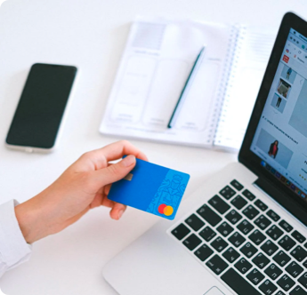 A person is holding a credit card in front of a laptop