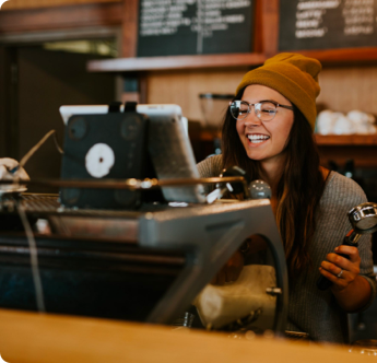 A woman wearing glasses and a beanie is sitting at a counter in front of a computer.