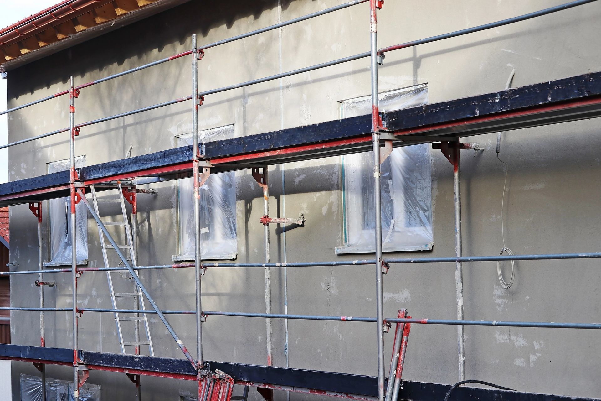 Facciata dell'edificio avvolta da impalcature e teli di plastica durante i lavori di ristrutturazione esterna.