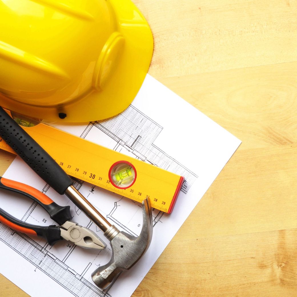 Attrezzi da costruzione e progetto su un tavolo di legno, con un elmetto giallo e una livella.