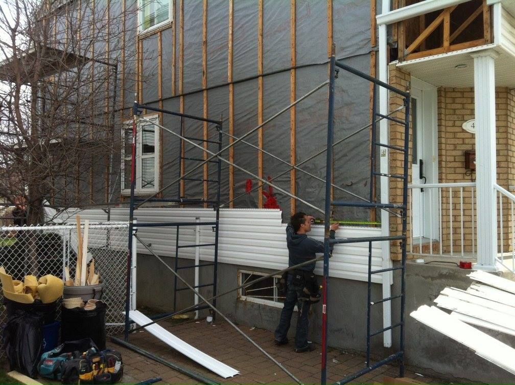 Un homme se tient sur un échafaudage devant une maison