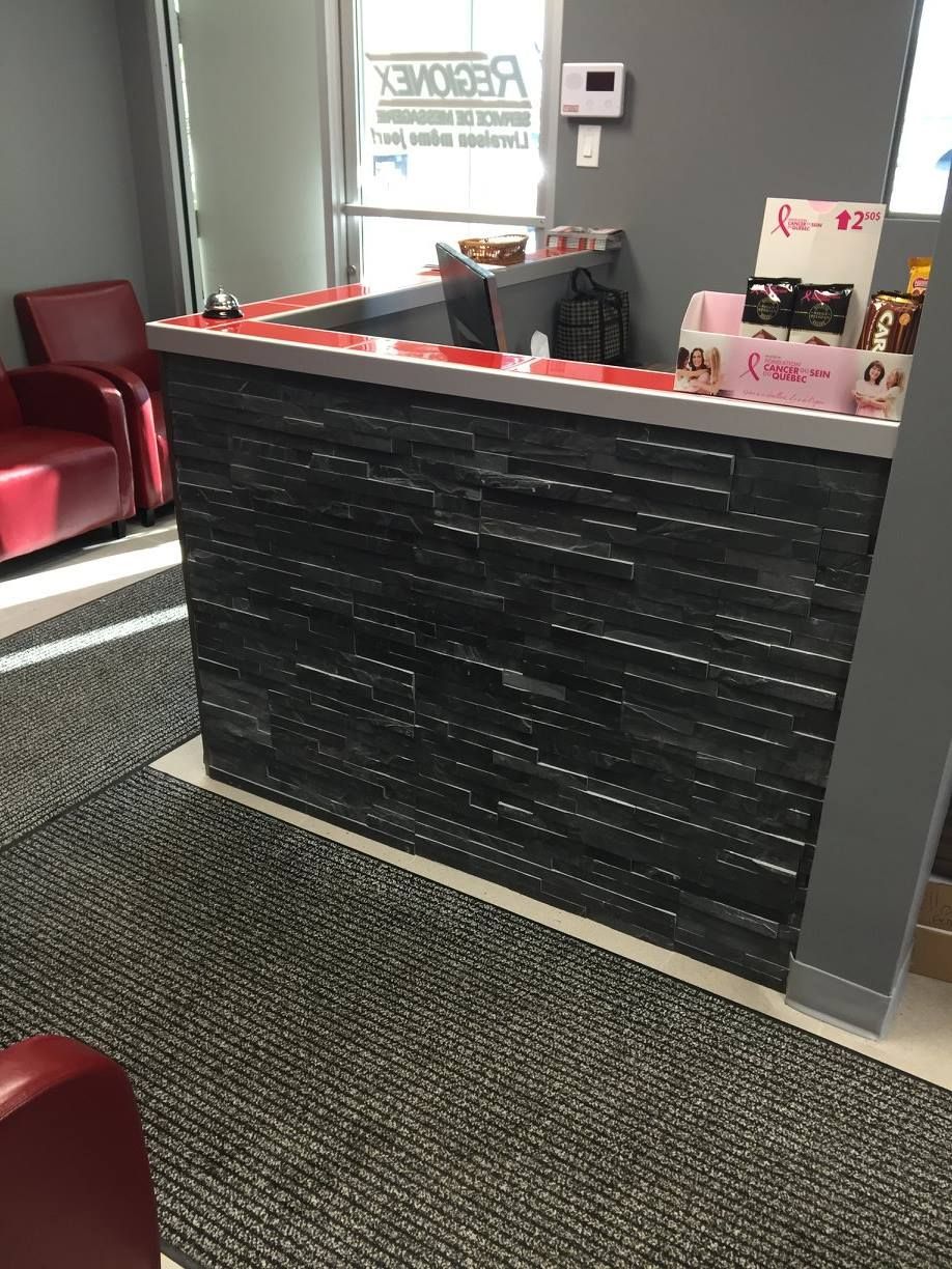 Une salle d'attente avec un comptoir noir et des chaises rouges.