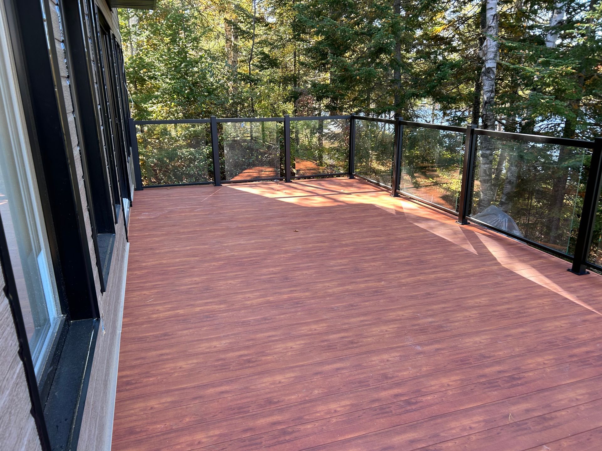 Une terrasse en bois avec une balustrade en verre et des arbres en arrière-plan.