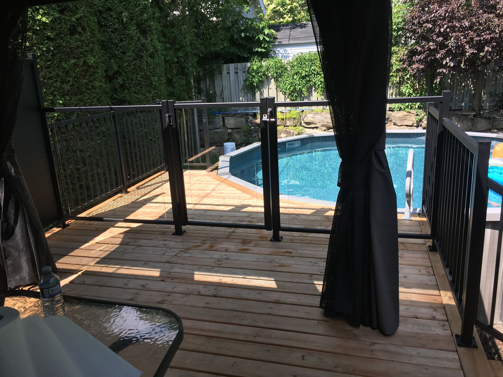 Une terrasse en bois avec une balustrade en verre donnant sur une piscine.
