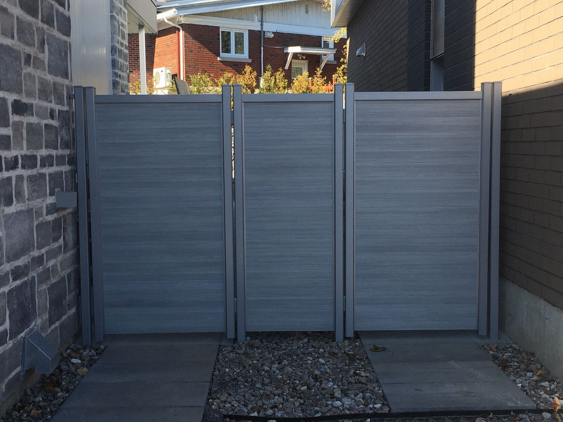 Une clôture grise se trouve devant un bâtiment en briques.