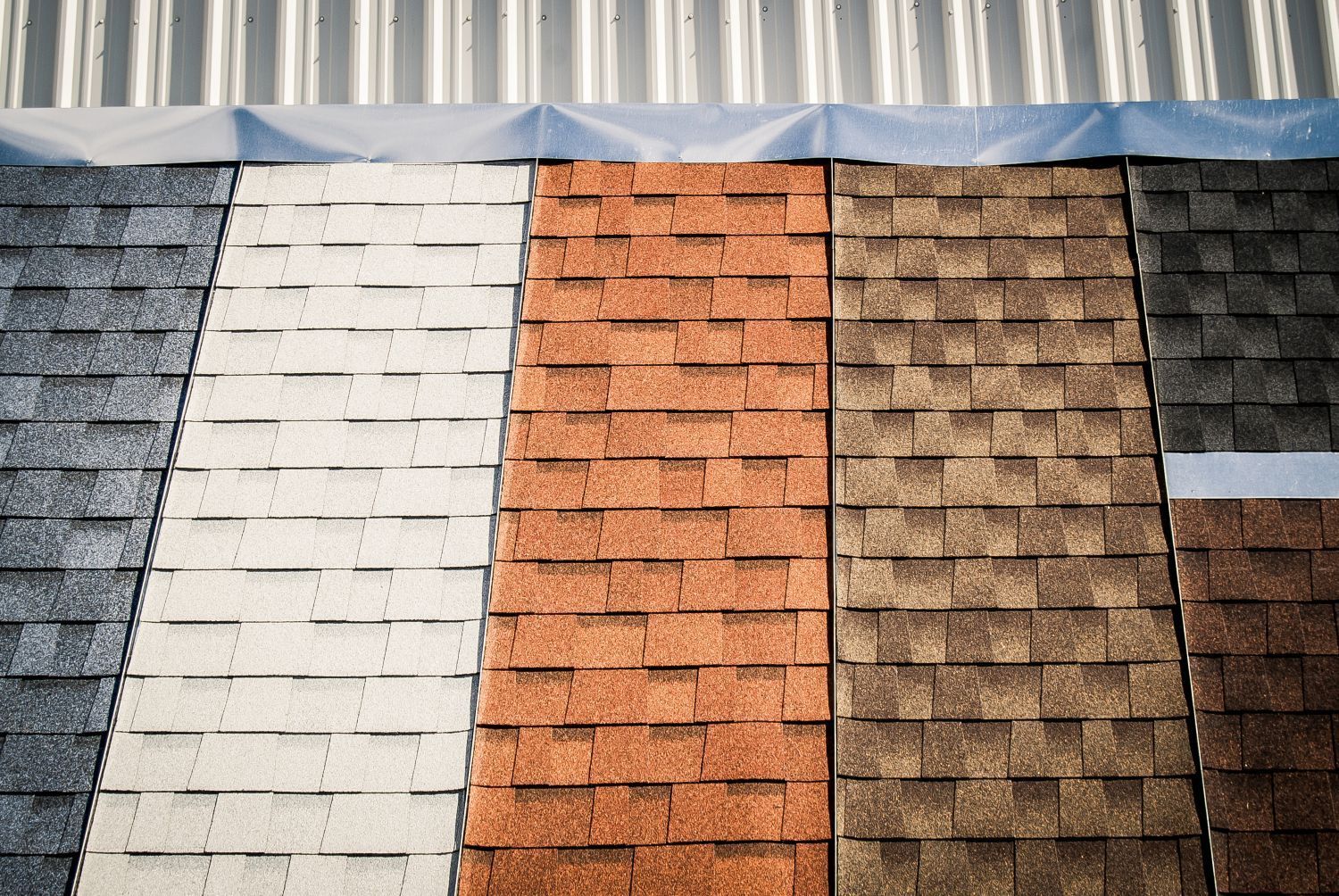 Various colored asphalt roofing shingle samples displayed under a metal roof.