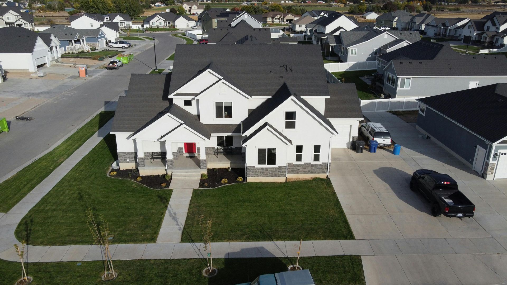 White two-story house with dark gray roof, on a green lawn, in a suburban neighborhood.