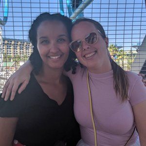 Two women are posing for a picture in front of a ferris wheel.