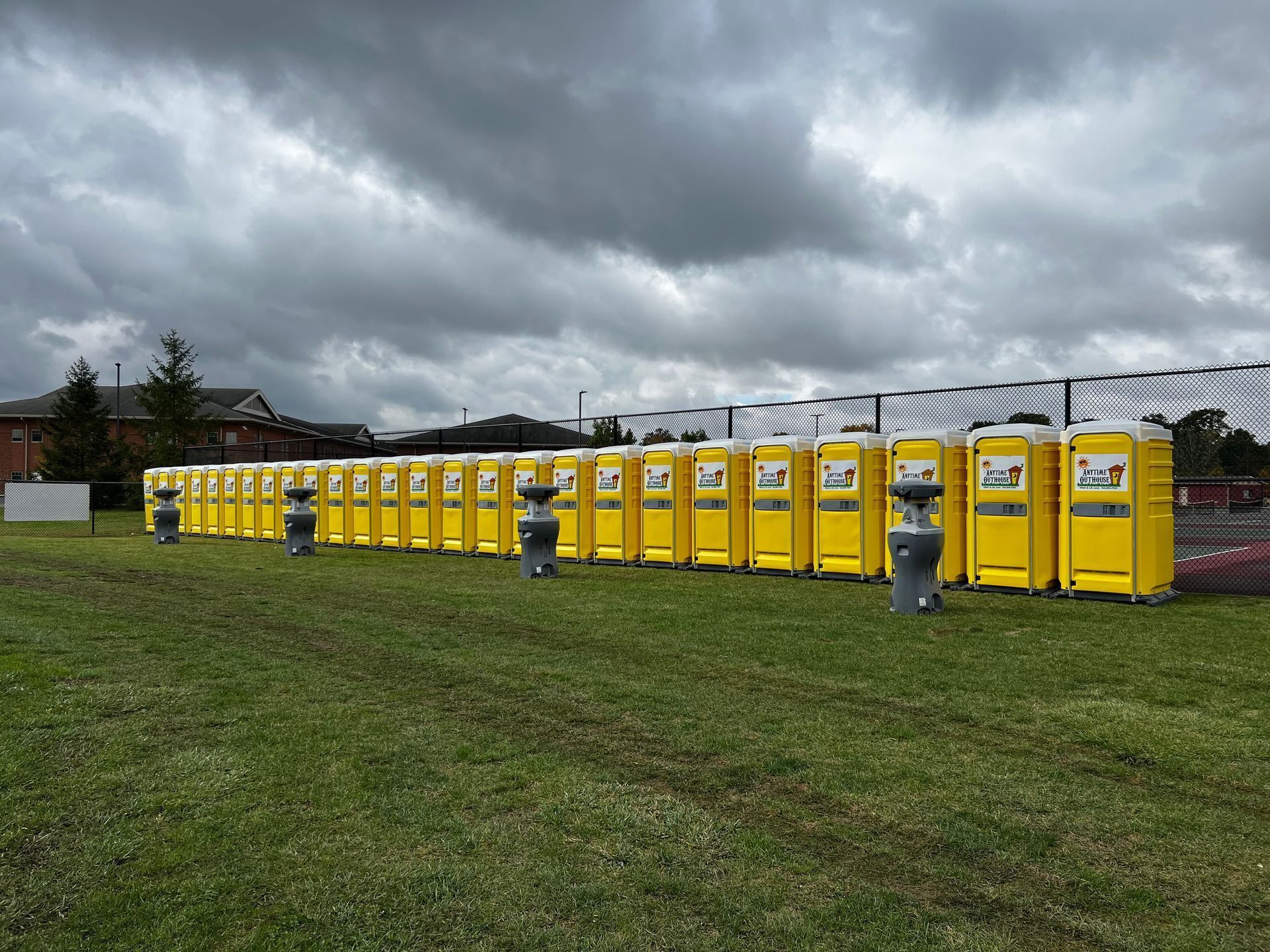 Row of yellow portable toilets on a grassy field under a cloudy sky.