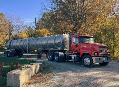 Red Mack truck with a silver tanker trailer and a Anytime Outhouse logo.