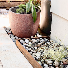A Potted Plant Is Sitting On Top Of A Pile Of Rocks Next To A Building — Creative Landscapes Coffs Harbour In Korora, NSW