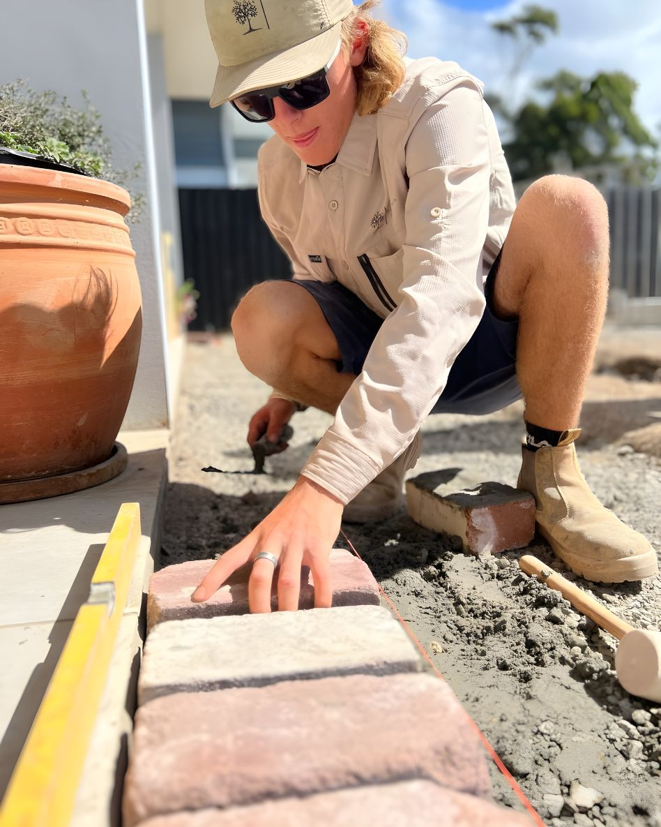 A Man Is Kneeling Down And Laying Bricks On The Ground — Creative Landscapes Coffs Harbour In Woolgoolga, NSW