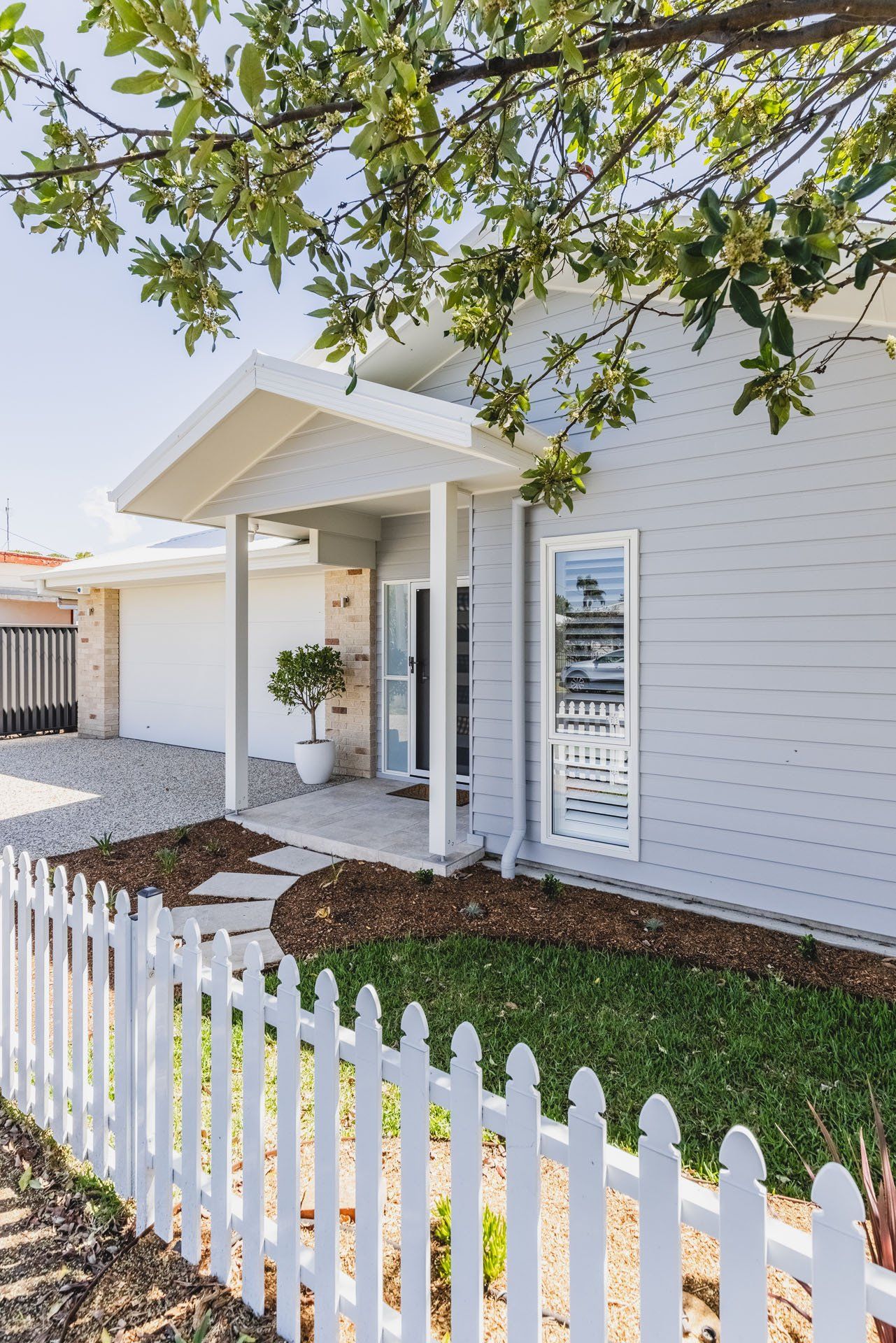 A White Picket Fence Surrounds A House With A Porch — Creative Landscapes Coffs Harbour In Korora, NSW