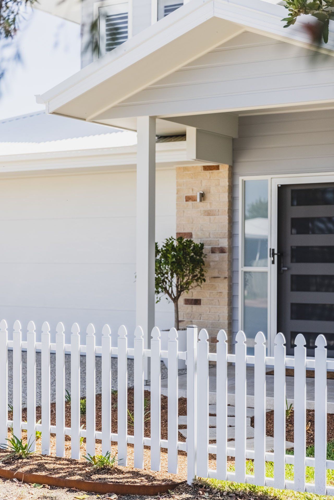 A White Picket Fence Is In Front Of A White House — Creative Landscapes Coffs Harbour In Korora, NSW