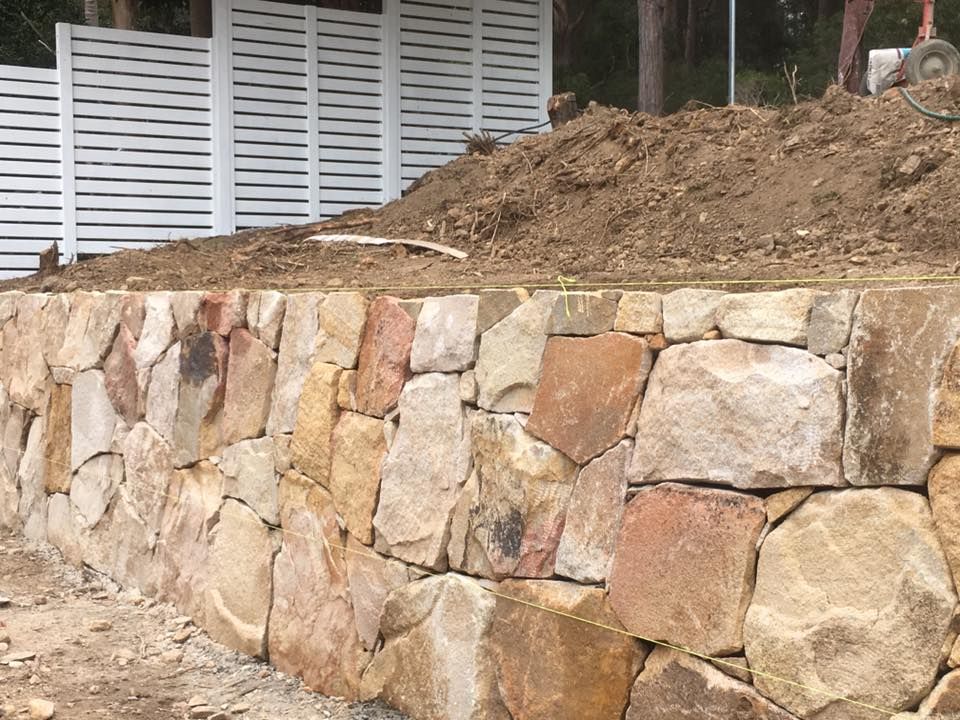 A Stone Wall Is Being Built On Top Of A Dirt Hill — Creative Landscapes Coffs Harbour In Korora, NSW