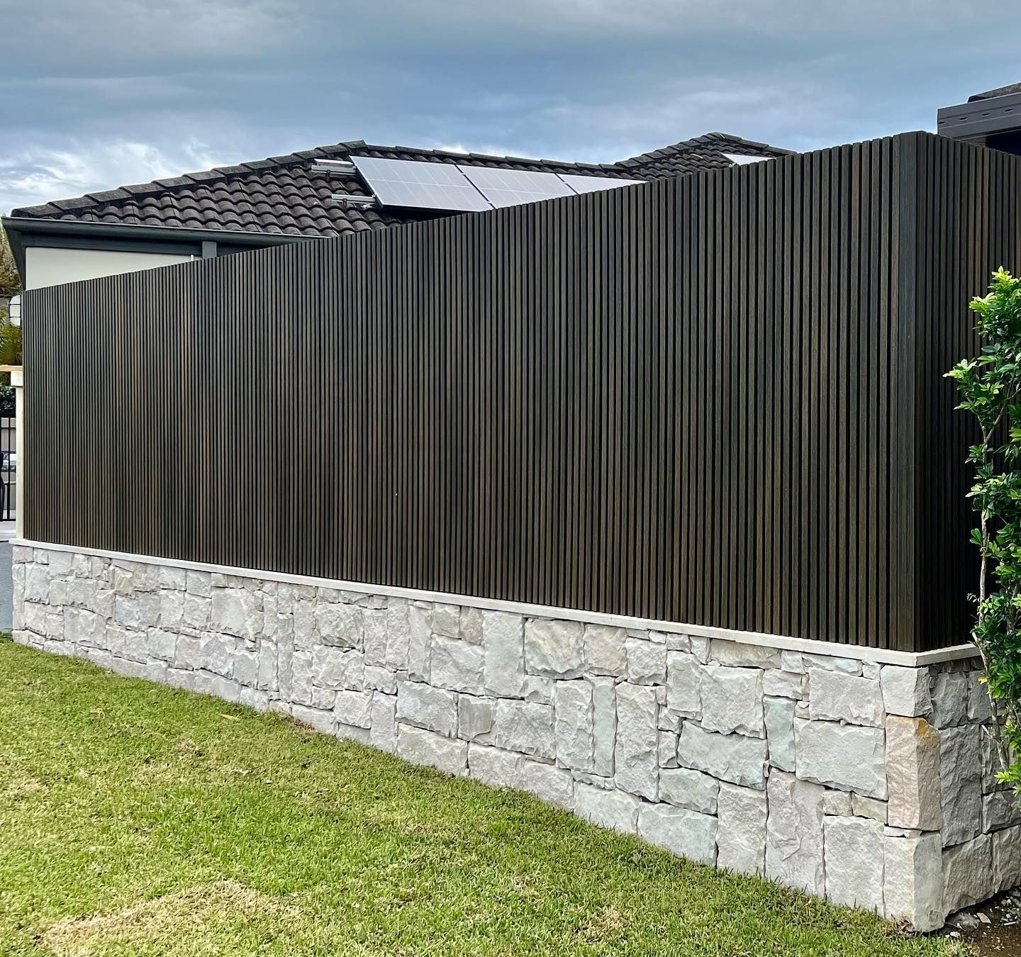 A Wooden Fence Surrounds A Stone Wall In Front Of A House — Creative Landscapes Coffs Harbour In Korora, NSW