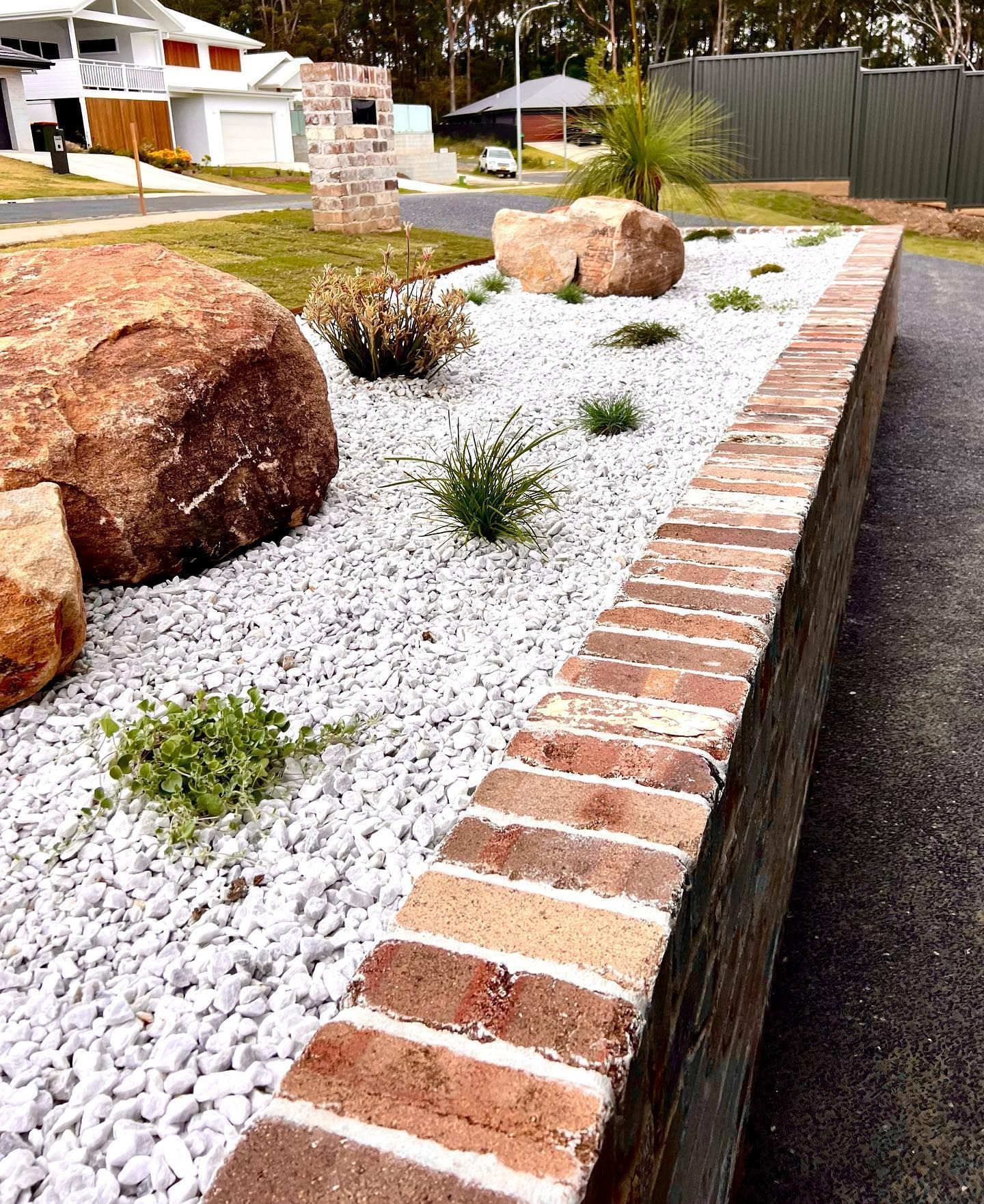 A Brick Wall Surrounds A Garden Filled With White Gravel And Rocks — Creative Landscapes Coffs Harbour In Korora, NSW