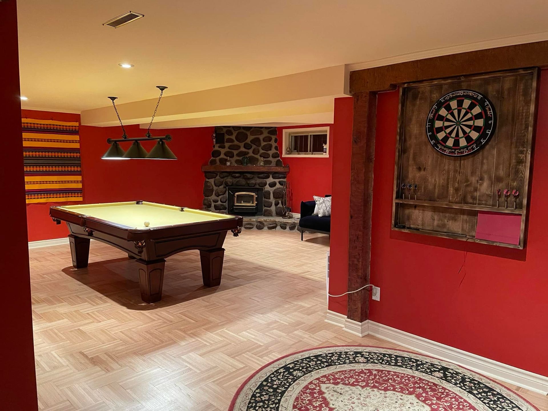 Sous-sol avec table de billard, cheminée, jeu de fléchettes et murs rouges.