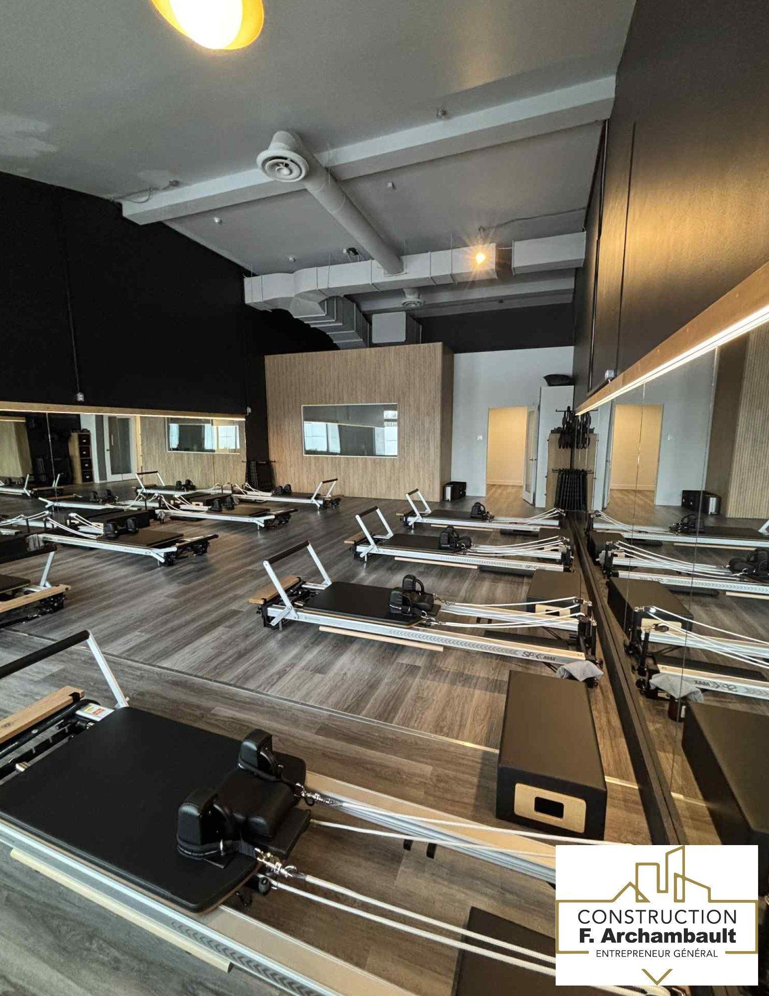 Studio de Pilates avec appareils Reformer. Sol en bois, murs noirs, miroirs.