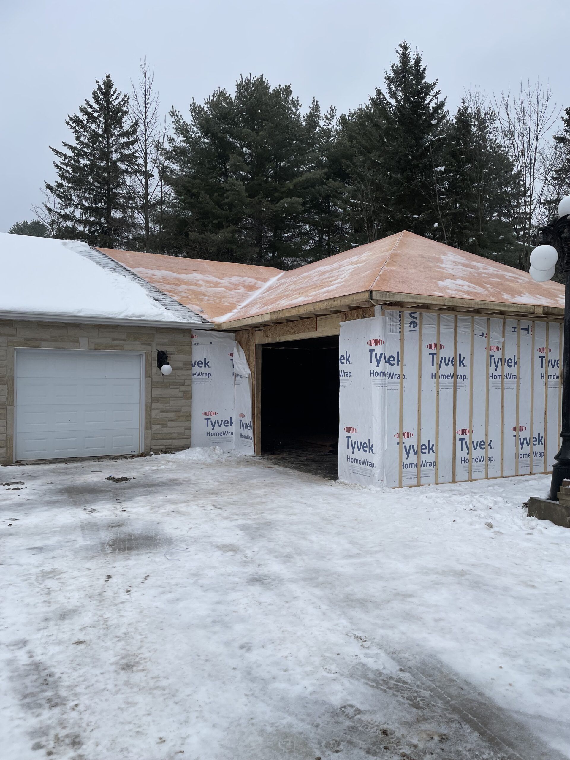Garage en construction dans un décor enneigé ; charpente et toit en bois visibles, porte latérale ouverte.