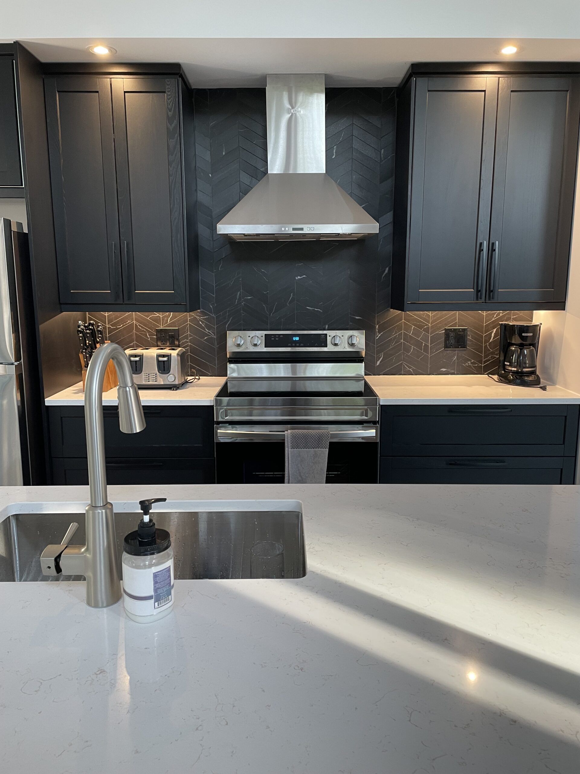 Cuisine équipée d'armoires gris foncé, d'appareils électroménagers en acier inoxydable et d'une crédence mouchetée.