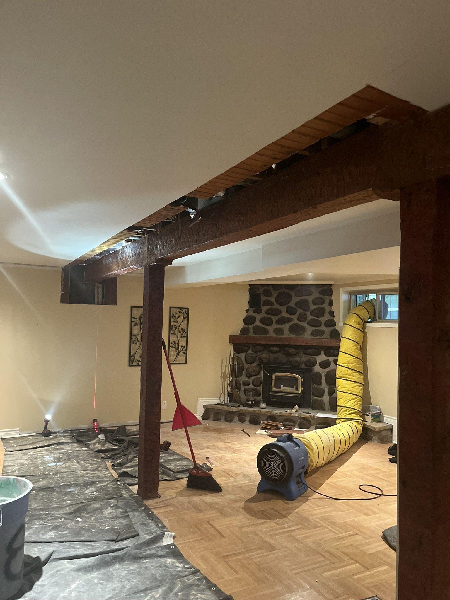 Sous-sol en cours de rénovation, avec poutres apparentes, cheminée et système de ventilation.