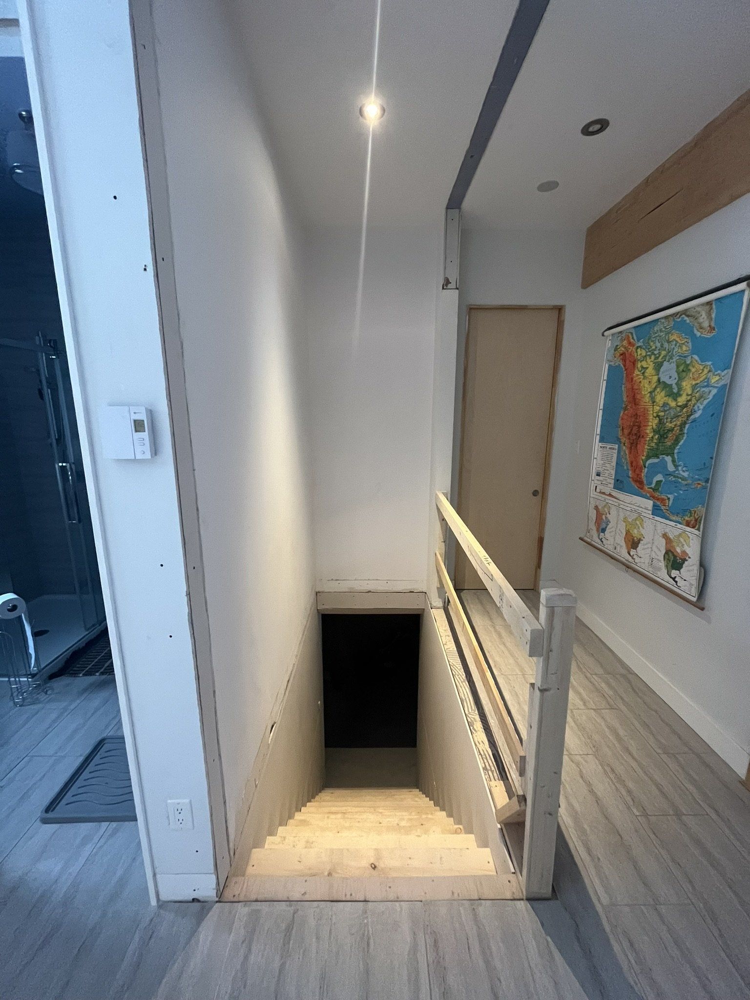 Un escalier descend vers une zone sombre, avec une rampe blanche et une carte du monde au mur.