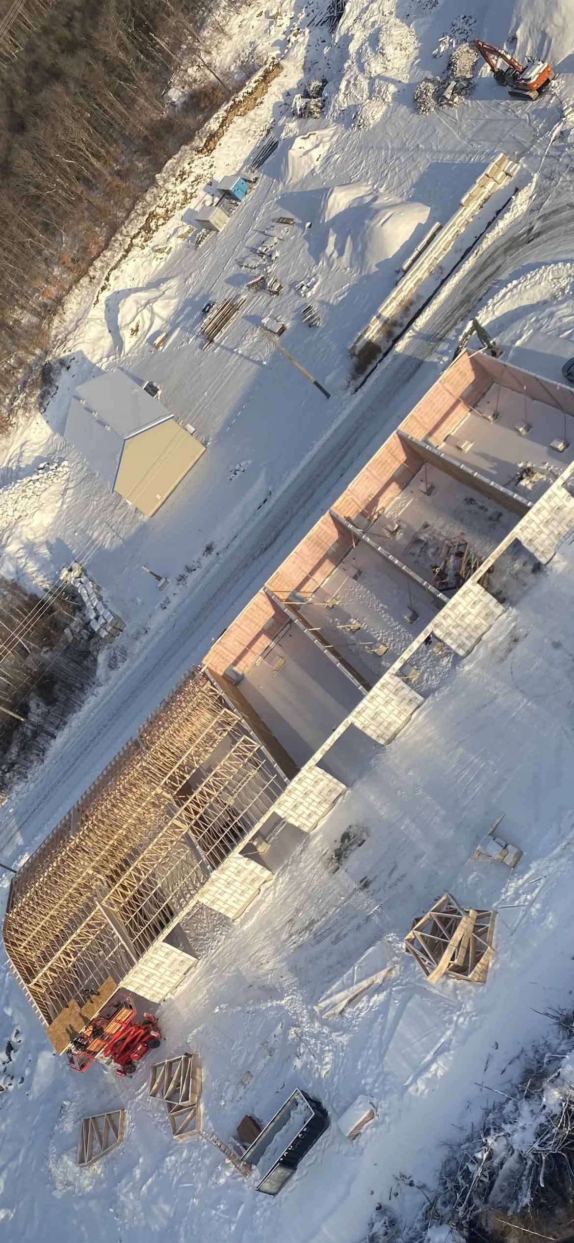 Vue aérienne d'un chantier de construction rectangulaire avec du bois à l'intérieur, entouré de neige.