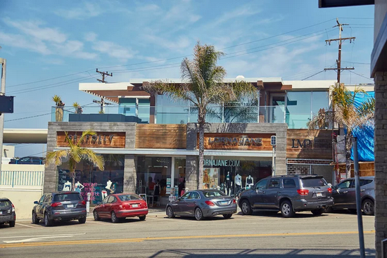 A modern retail building with wood accents and a second-story balcony, fronted by a parking lot with several parked cars.