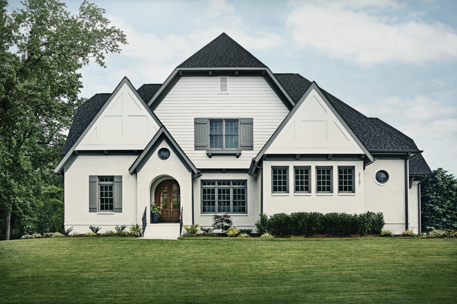 A large white house with a black roof is sitting on top of a lush green field.