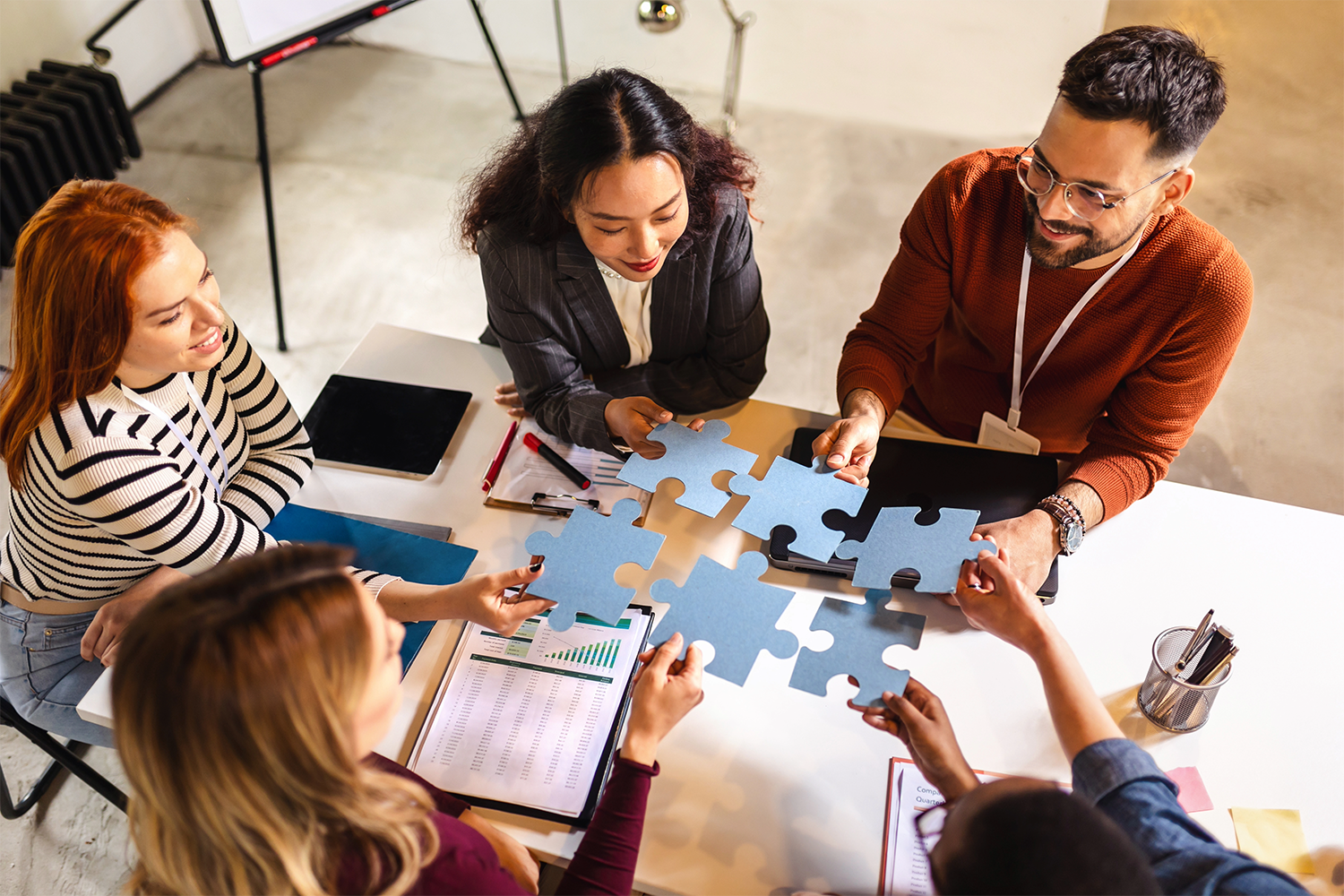 A group of people are sitting around a table putting together a puzzle.