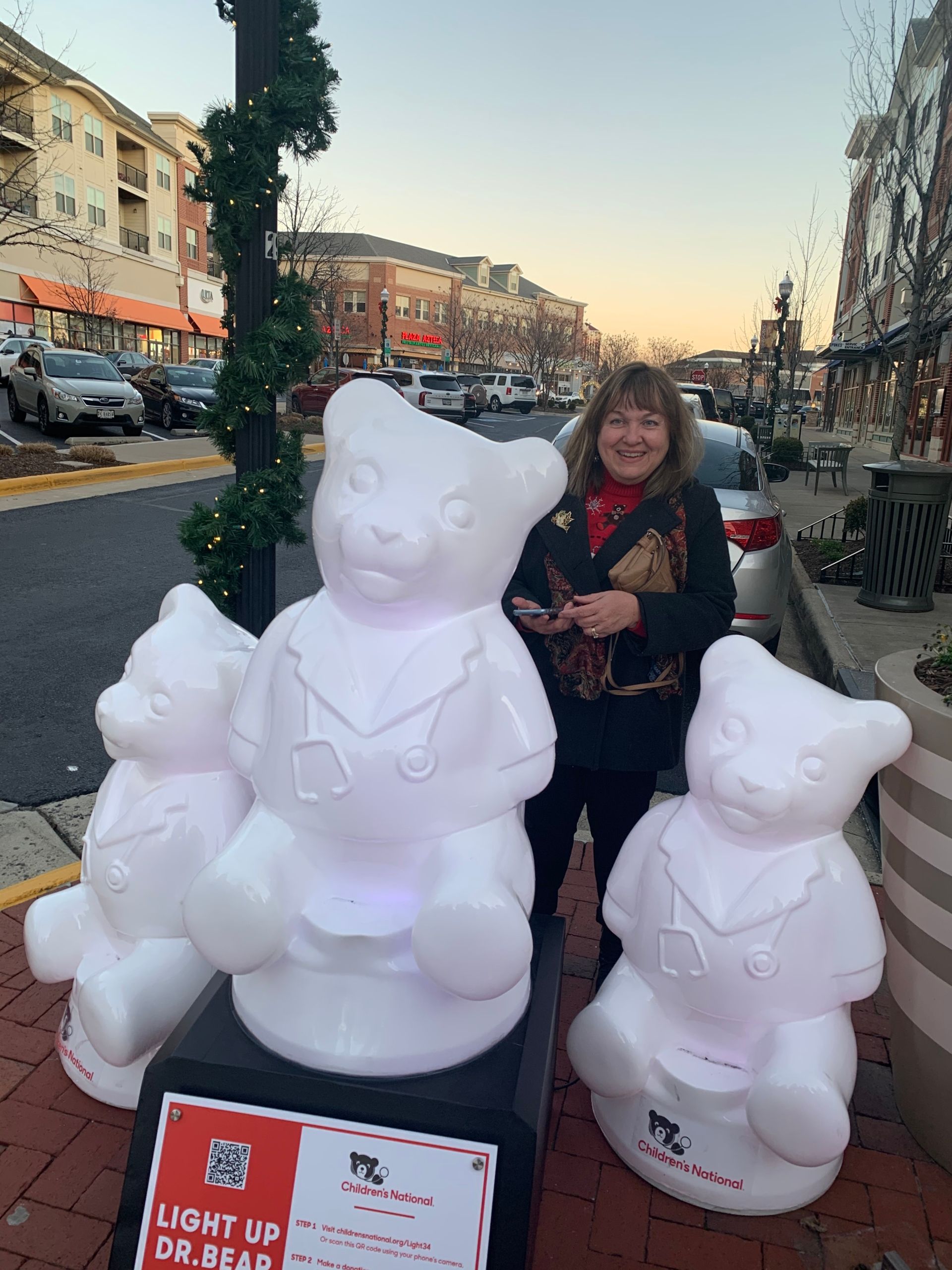 A woman is standing next to three white teddy bears on a sidewalk.