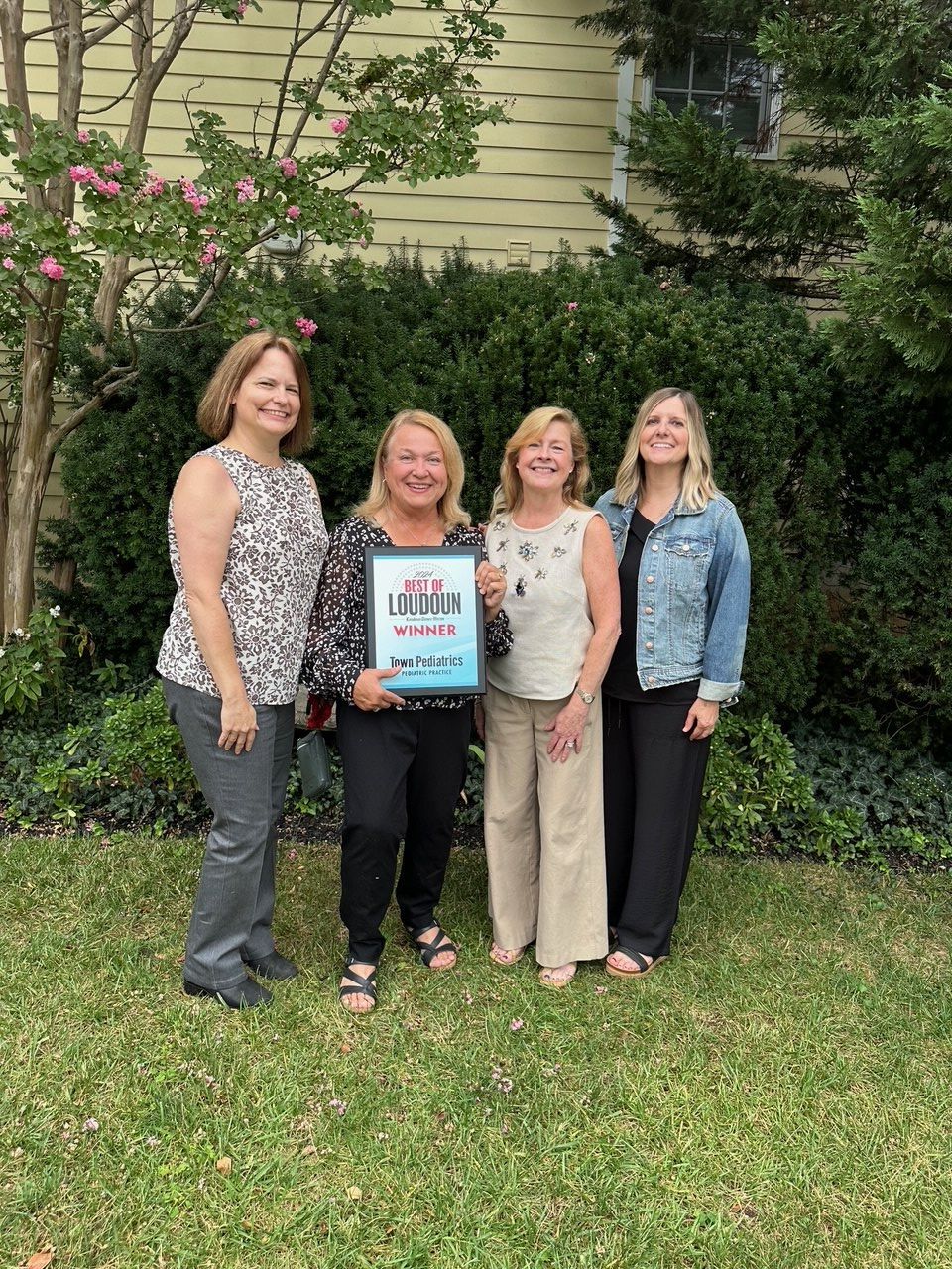 A group of women are standing in a grassy field holding a sign.