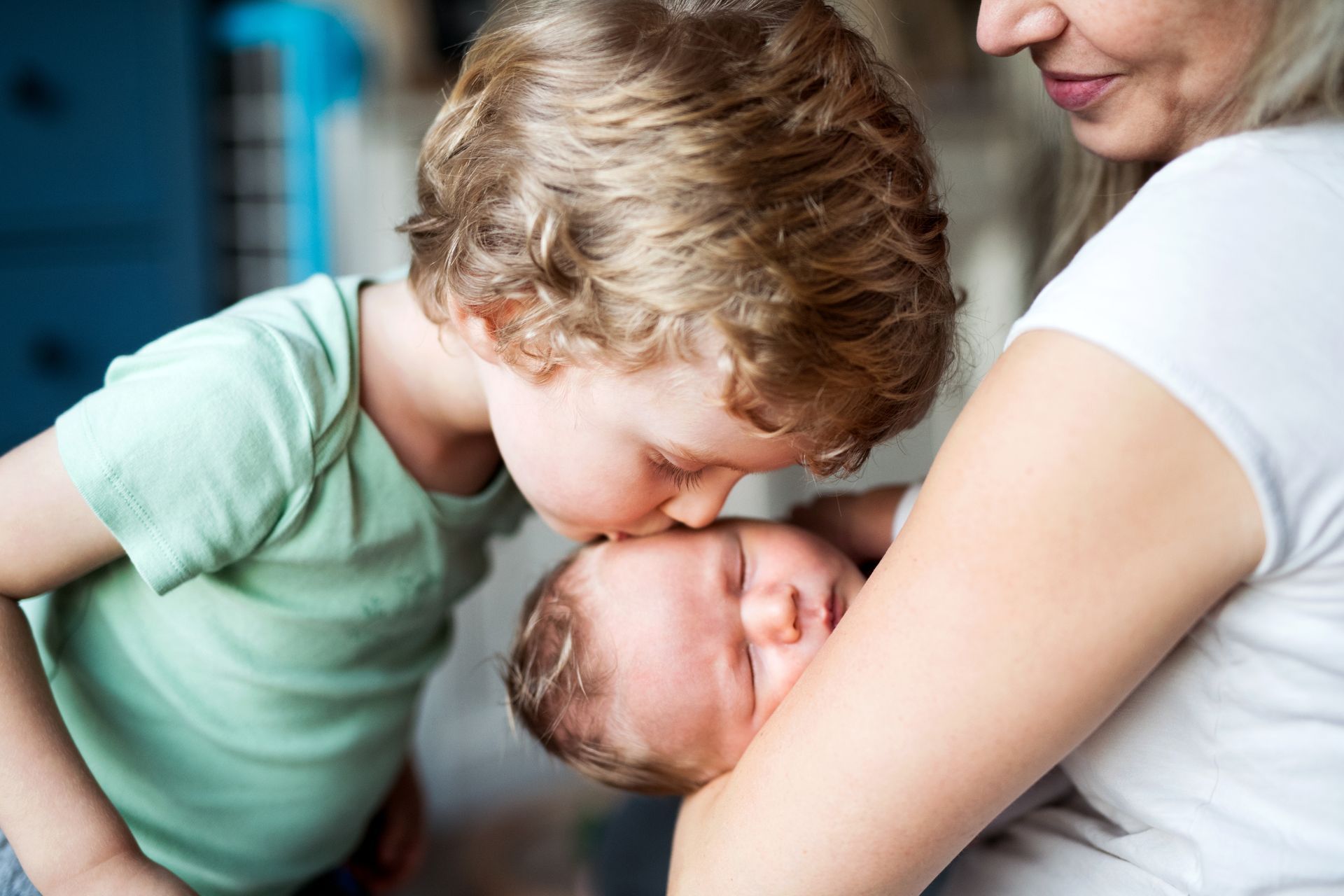 Mother holding sleeping baby and boy kissing the baby's head.