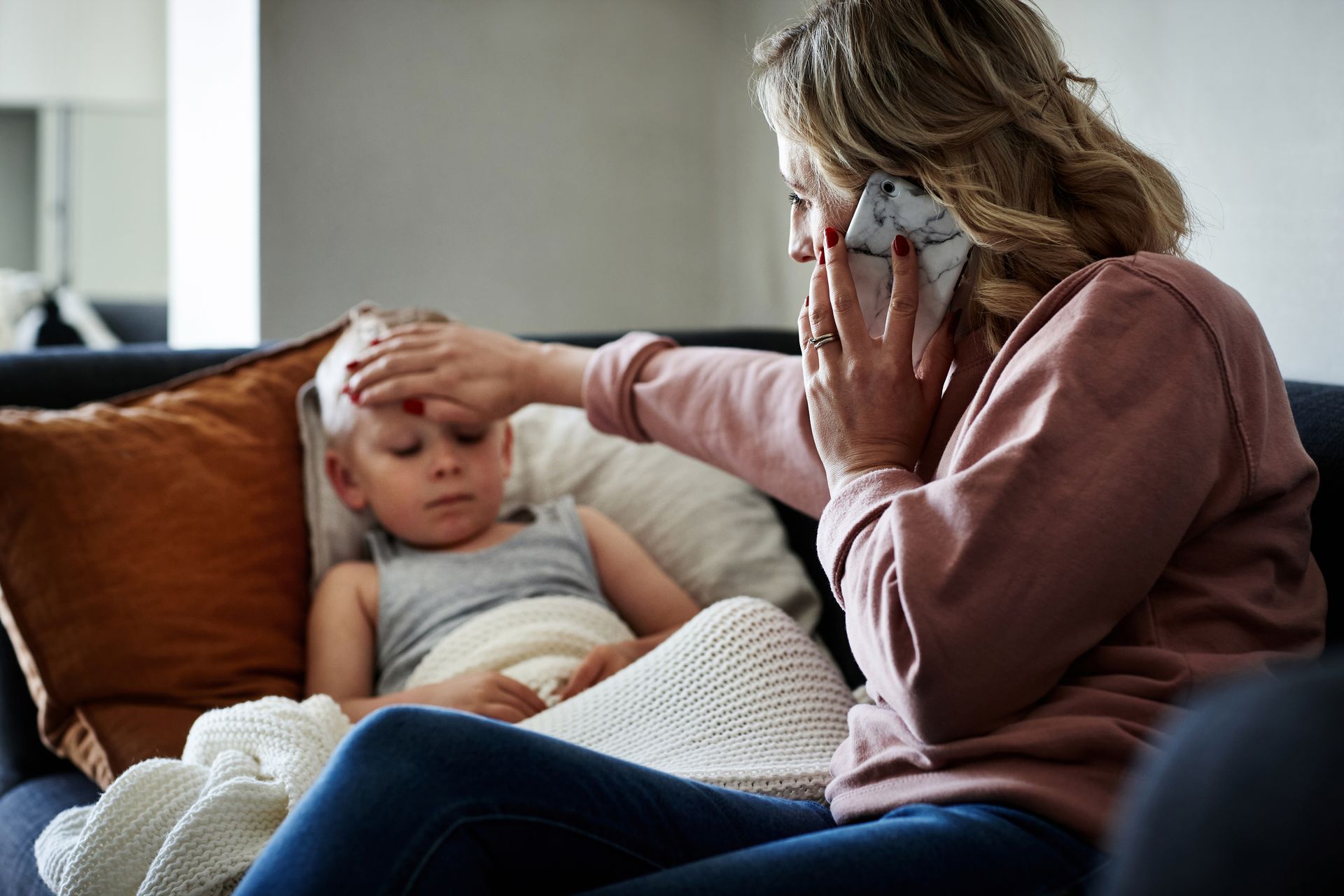 A woman is sitting on a couch with a sick child and talking on a cell phone.