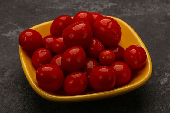 A yellow bowl filled with red cherry tomatoes on a table.