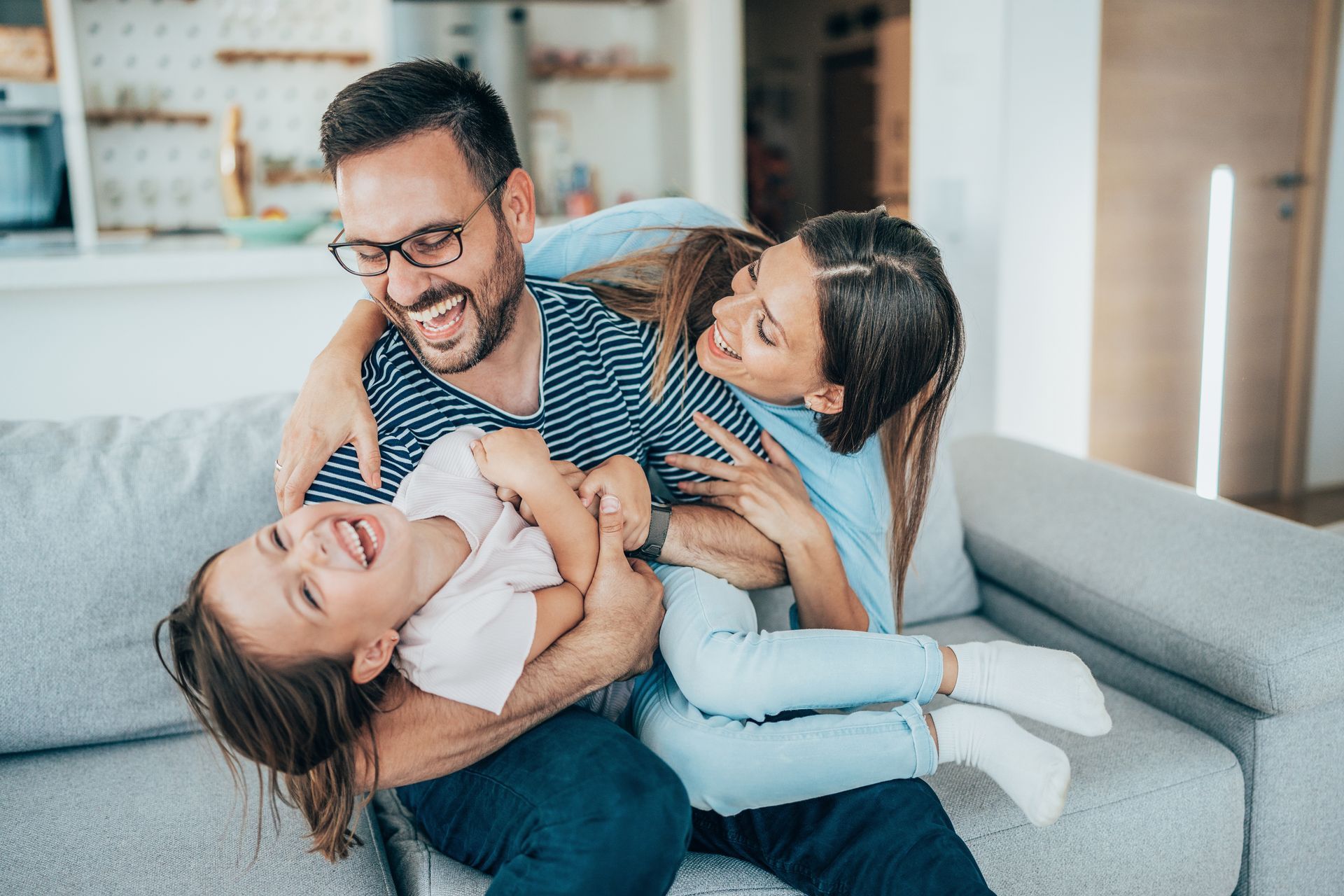 Mother, father and daughter sitting on couch, laughing. 