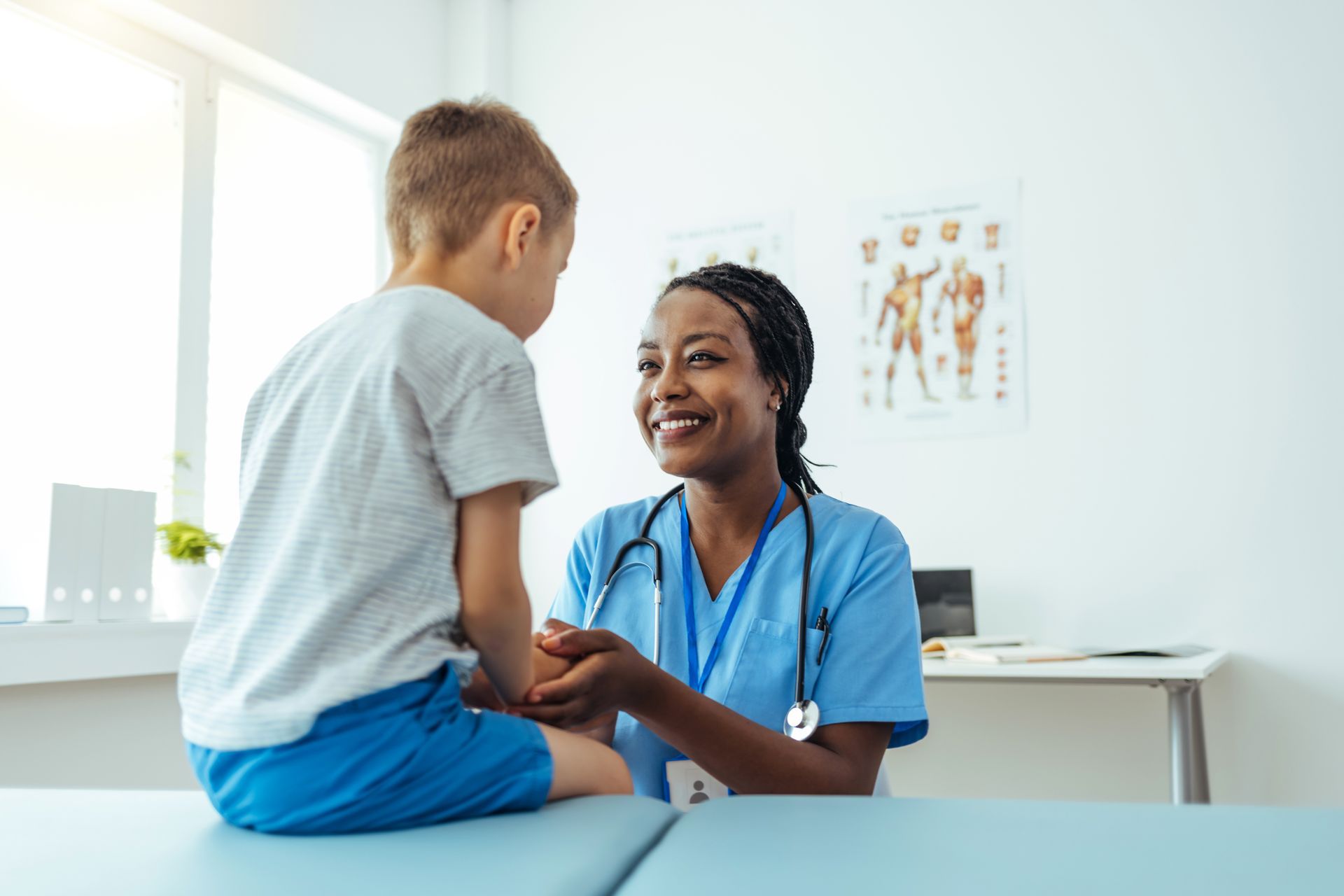 A female medical professional is holding the hand of a young boy in a hospital.