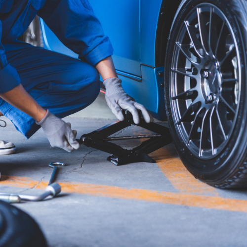 A man is using a jack to change a tire on a blue car.