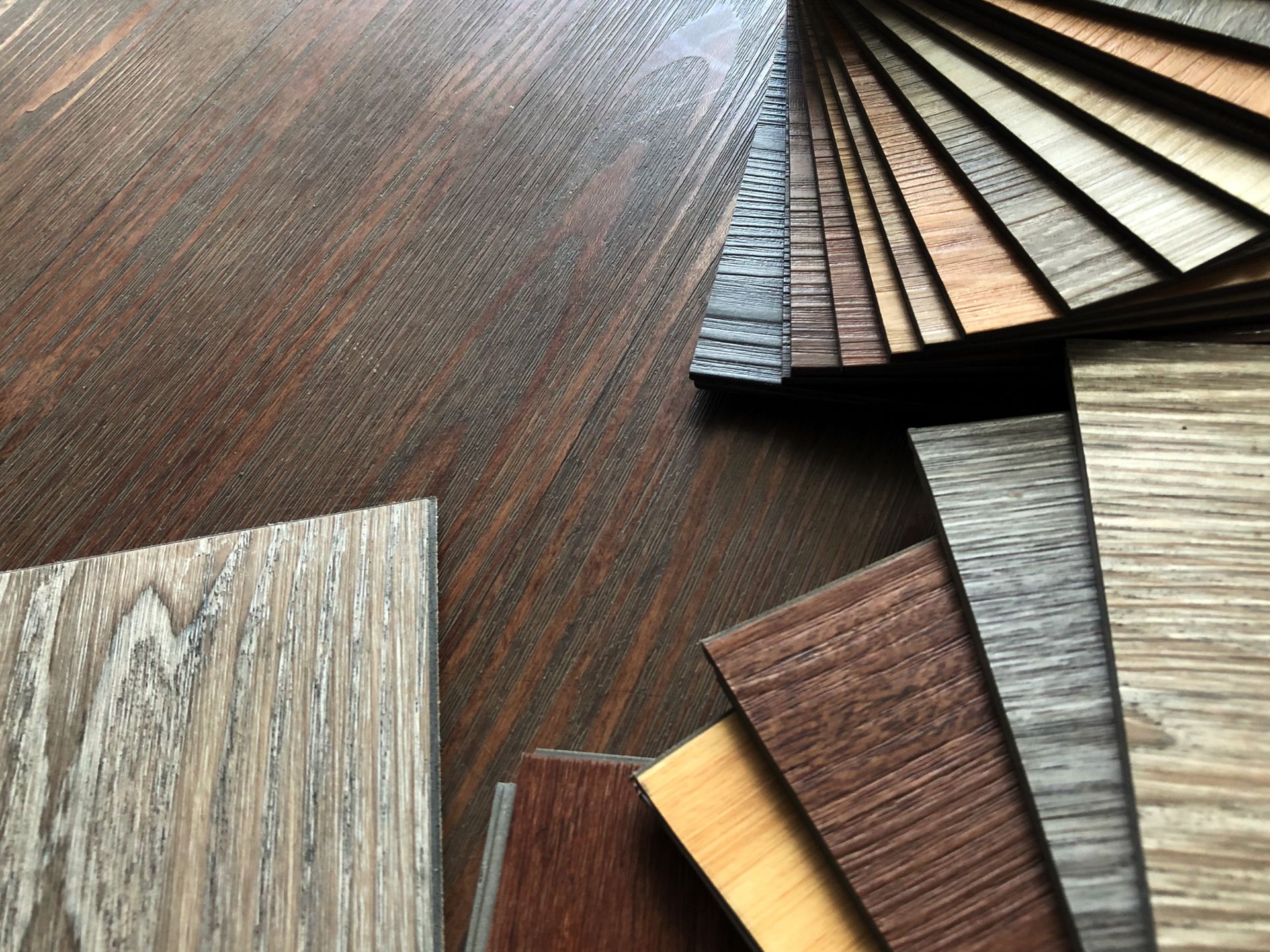 Wood flooring samples fanned out on a dark wood tabletop, showing assorted grain and stain colors