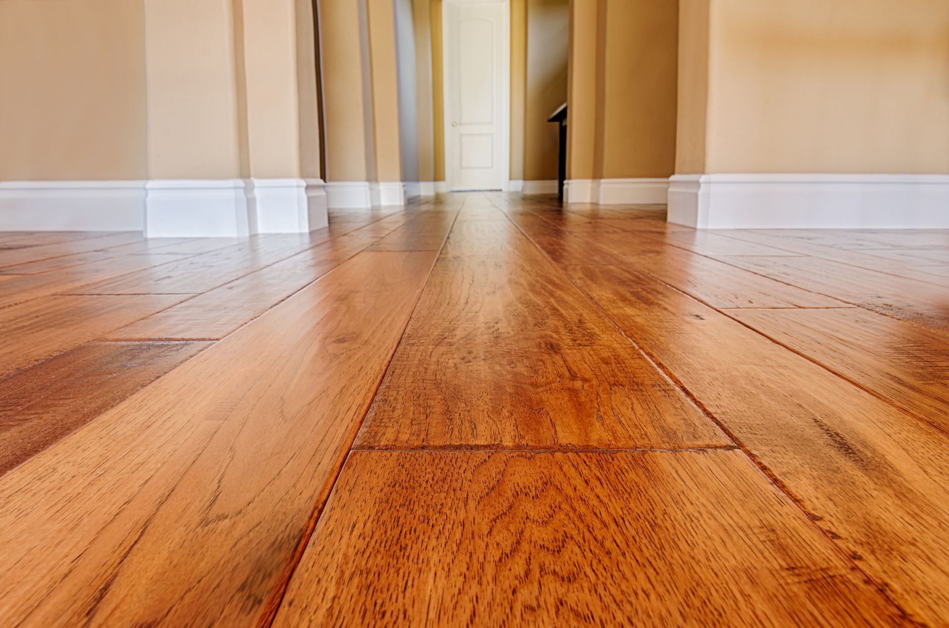 Empty hardwood hallway with warm tan walls and white trim, viewed from floor level.