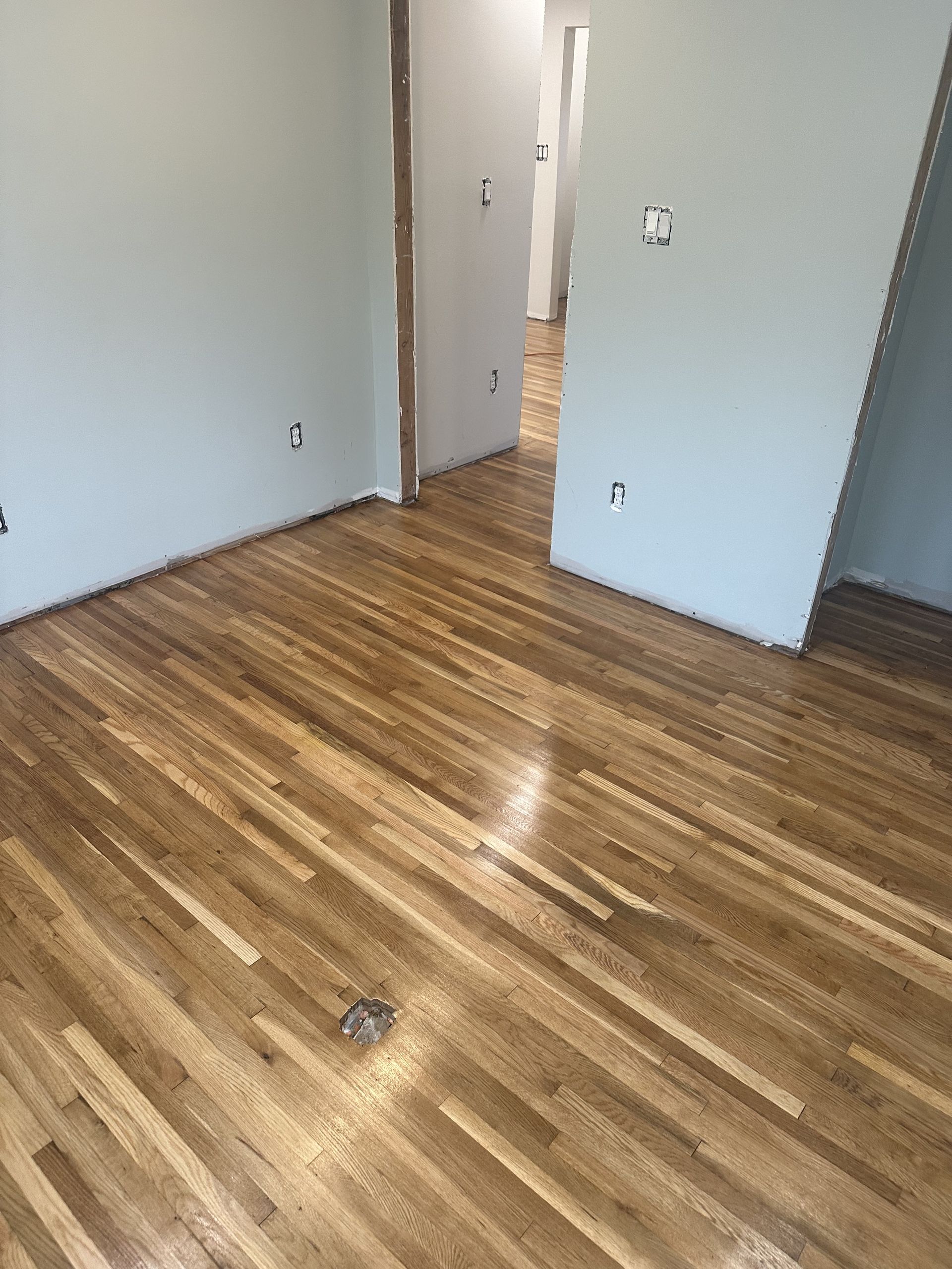 Empty room with wood flooring, pale walls, and an open doorway to a hallway