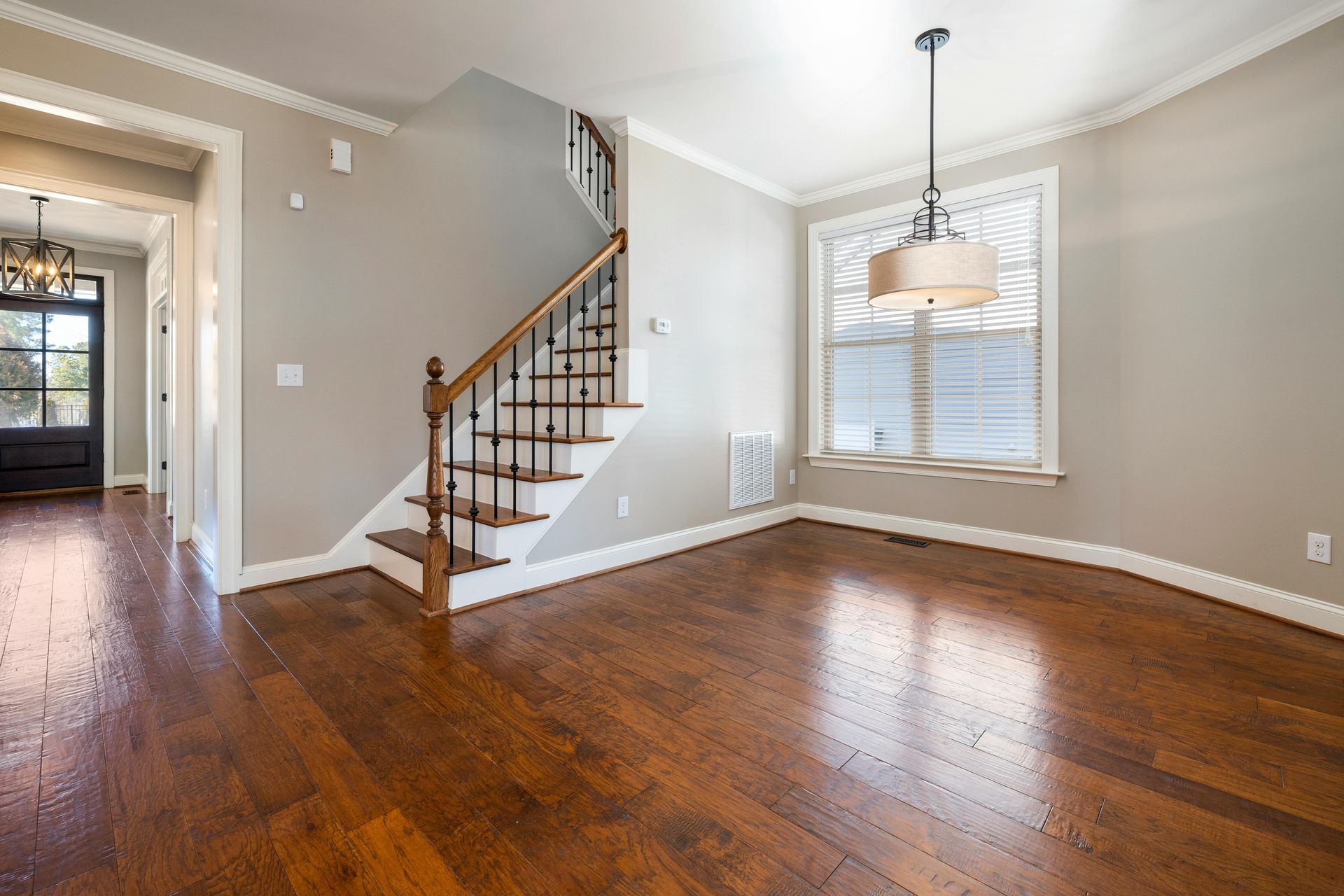 Empty dining room with hardwood floors, staircase, and chandelier.