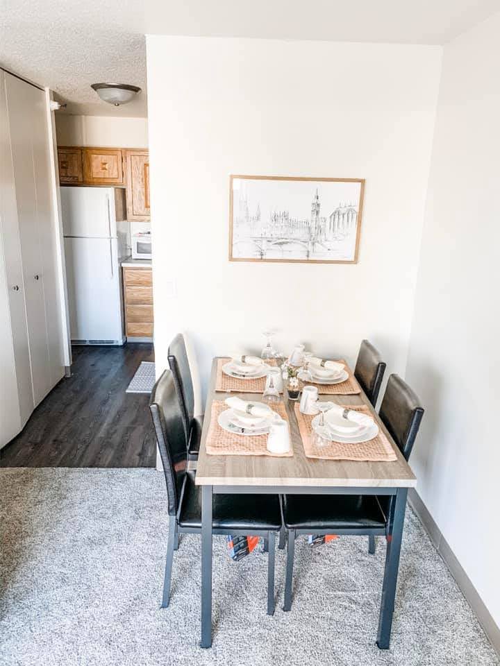 Interior view of apartment dining area example with light gray carpet, dining table with four chairs, adjacent to the kitchen.