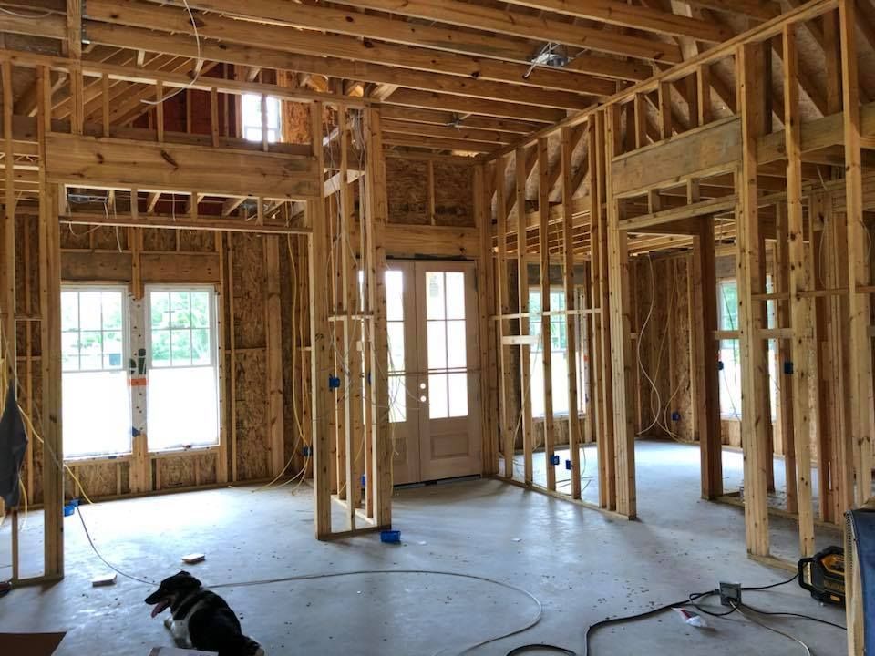 Interior of a house under construction. Wooden framing is visible, with a dog on the concrete floor.