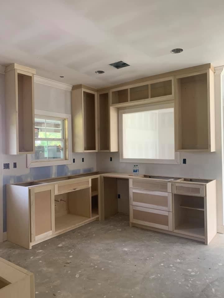 Unfinished kitchen with light-colored cabinets, countertop space, and a window. Concrete floor.