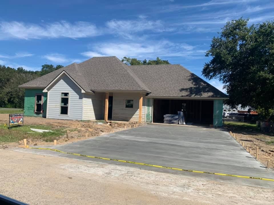 New house under construction with a concrete driveway on a sunny day.