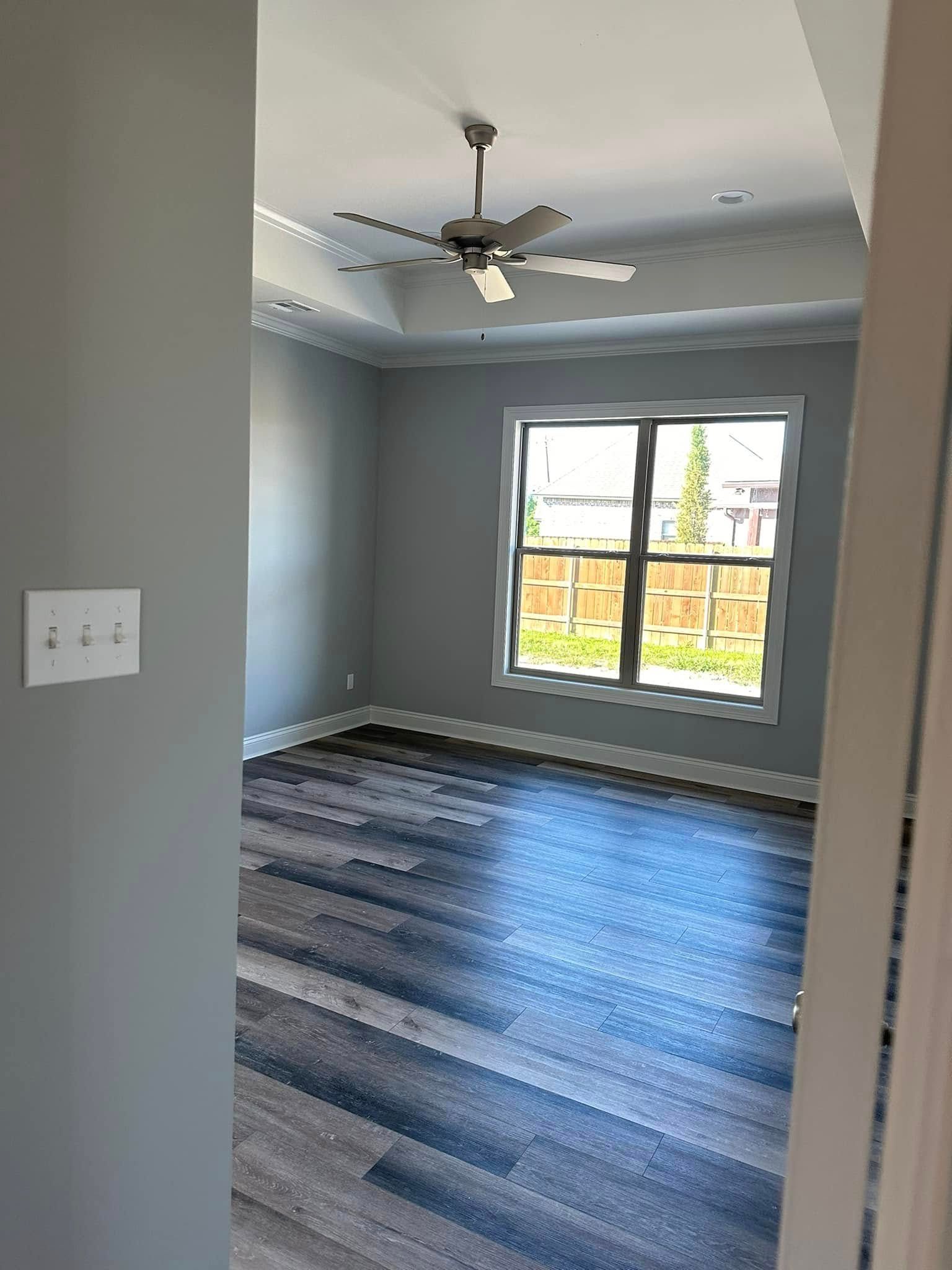 Empty room with gray walls, wood-look floor, window, ceiling fan.