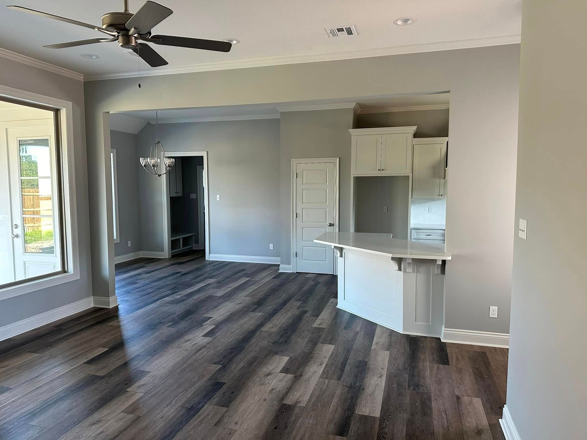 Open-concept living space with dark wood flooring, gray walls, and white kitchen cabinets.